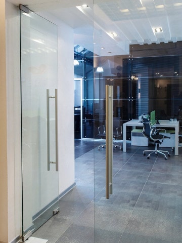 Цельностеклянные маятниковые двери в офисном помещении